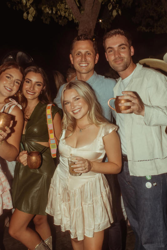Group of friends, man and women, hug and pose for a picture holding drinks
